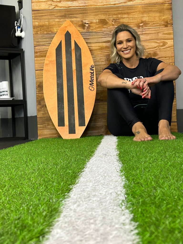 Gestora Mari do Studio Mormaii Morumbi sentada sorrindo no chão ao lado do equipamento Spin no dia da inauguração da unidade